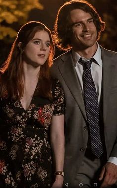 a man in a suit and tie standing next to a woman wearing a floral dress