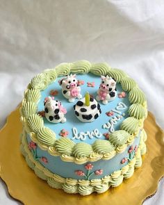 a blue and yellow cake with three small cows on it's top sitting on a gold platter