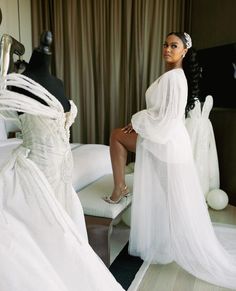 a woman in a white dress sitting on a bed next to mannequins