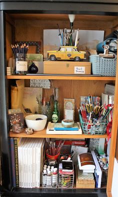 an open bookcase filled with lots of books and office supplies on top of it