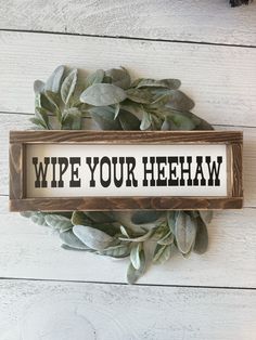 a wooden sign that says wipe your hehaw on it next to some leaves