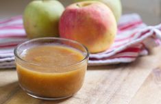 an apple and orange juice in a small glass on a wooden table next to apples