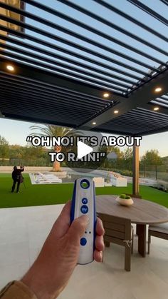 a hand holding a remote control in front of a patio with a table and chairs