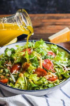 a salad in a bowl with dressing being poured into it and cheese on the side