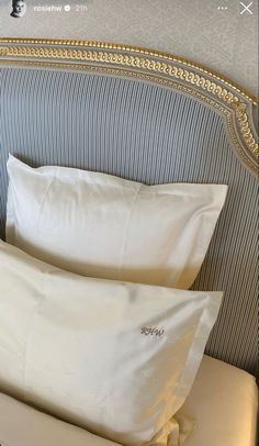 two white pillows sitting on top of a bed next to a headboard with gold trim