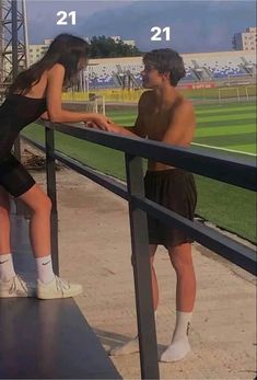 a man and woman leaning against a rail at a baseball field with the sky in the background