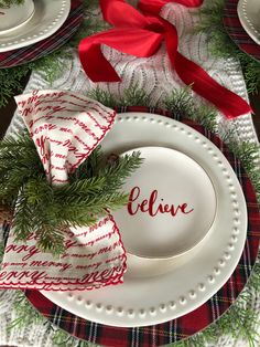 a christmas place setting with red and white napkins, pine branches, and ribbon