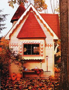 a white house with a red roof surrounded by fall leaves and pumpkins on the ground