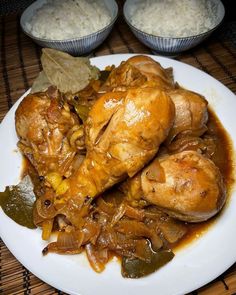 a white plate topped with chicken covered in gravy next to bowls of rice