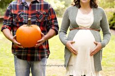 a man and woman standing next to each other in front of a field with an orange pumpkin