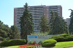 an apartment building in the background with trees and flowers on the grass around it's edges