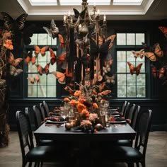 a dining room table is set with orange flowers and butterflies on the wall behind it