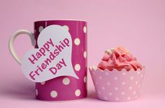 a pink cupcake next to a pink and white mug with the words happy friends day written on it