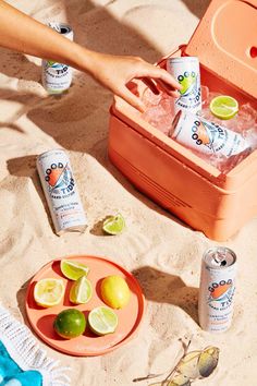 a cooler with lemons and limes on the beach next to it, surrounded by other drinks