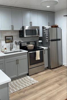 a kitchen with stainless steel appliances and white counter tops, wood flooring and gray cabinets