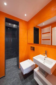 a bathroom with an orange wall and white sink, toilet and stand up shower stall