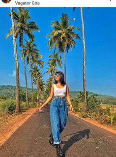 a woman walking down the middle of a road with palm trees in the back ground