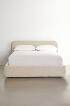 a white bed with two pillows on top of it next to a wall and floor