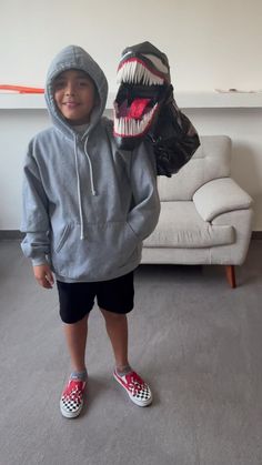 a young boy wearing a gray hoodie and black shorts with a dinosaur mask on his face