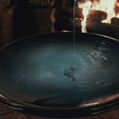 a large metal bowl sitting on top of a table next to a fire place with flames in the background