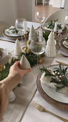 the table is set with white plates and silverware, greenery and candlesticks