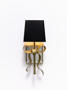 a wall mounted lamp with a black shade on it's side and a gold bow around the base