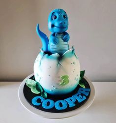 a blue and white cake with a dinosaur on it's top sitting in an egg shell