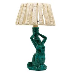 a table lamp with a green mermaid sitting on it's side and a beige shade