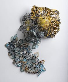 two pieces of art made out of glass and wire on a white surface, one piece is yellow and the other part is blue