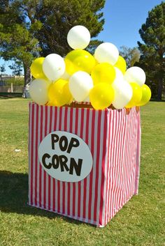 a popcorn bag filled with yellow and white balloons sitting on top of a grass covered field