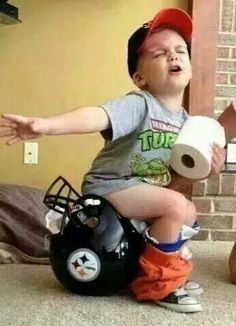 a young boy sitting on top of a football helmet holding a roll of toilet paper