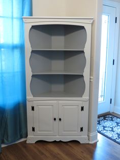 a white bookcase with two doors on the front and one door open to reveal a blue curtain