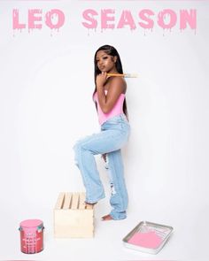 a woman in pink shirt and jeans leaning on wooden crate with paint cans next to her