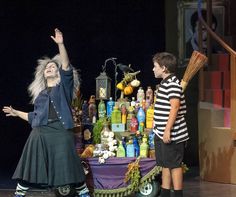 two people standing on stage with brooms in front of an arrangement of bottles and vases