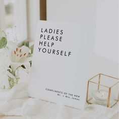 a card that says ladies please help yourself next to a candle and flowers on a bed