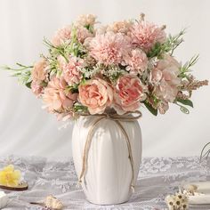 a white vase filled with lots of flowers on top of a lace covered table cloth