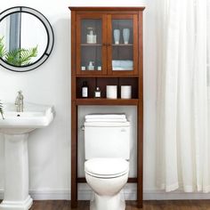 a white toilet sitting next to a sink and a wooden cabinet in a small bathroom