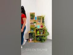 a woman standing in front of a wall filled with potted plants