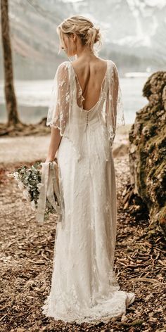 a woman in a white wedding dress standing on the beach with her back to the camera