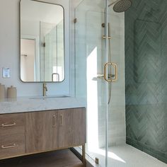 a bathroom with a walk in shower next to a white sink and wooden cabinetry