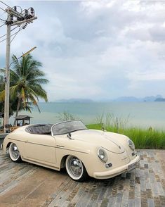 an old style car parked on the side of a road next to some water and palm trees