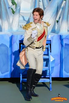 a man in a white suit and black boots standing next to a blue chair with an ice sculpture behind him