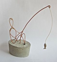 a wire sculpture on top of a cement block with a small bird hanging from it's back