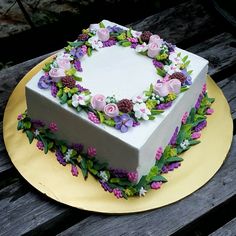 a square cake decorated with flowers and greenery on a yellow plate sitting on a wooden table