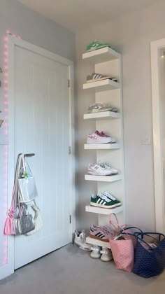 a white closet with several shelves filled with shoes and bags next to a door that has pink lights on it