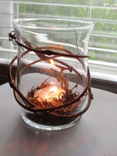 a candle is lit in a glass bowl with branches and twigs around it on a table next to a window