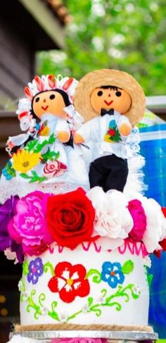 a colorful cake with two dolls on top and flowers in the bottom, sitting next to each other