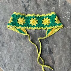 a green crocheted headband with yellow flowers on it sitting on a rock