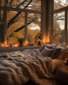 an unmade bed in front of a large window with candles on the windowsill