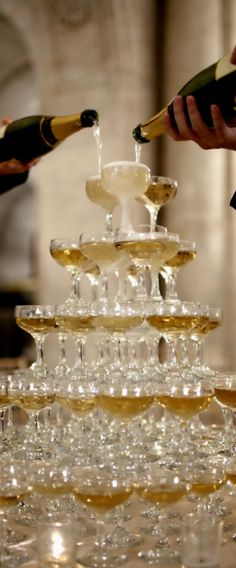 champagne being poured into wine glasses on top of a large cake stand in front of a fireplace